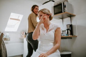 Braut im Spitzenkleid sitzt in der Küche, berührt und gerührt – Hochzeitsfotografin Köln hält den Moment fest.