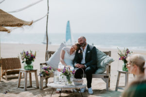 Brautpaar entspannt auf einer Bank am Meer, umgeben von Blumen – Hochzeitsfotografin Köln fängt echte Momente ein.