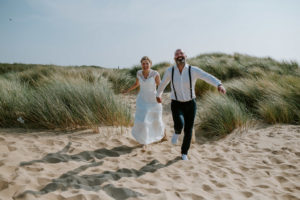 Brautpaar läuft lachend am Strand entlang – natürliche Hochzeitsfotos von eurer Hochzeitsfotografin Köln.