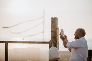 Ein Bräutigam läutet bei Sonnenuntergang am Strand eine Glocke, festgehalten von der Hochzeitsfotografin Köln.