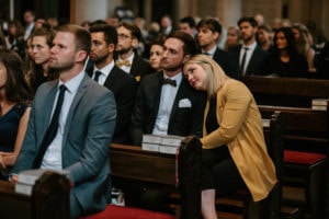 Die Gäste sitzen während der Zeremonie zusammen, während sich eine Frau in Gelb sanft an ihre Partnerin – die Hochzeitsfotografin Köln – lehnt.