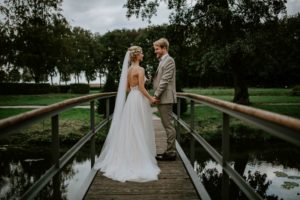 Brautpaar hält sich lächelnd an den Händen auf einer Holzbrücke – Hochzeitsfotografin Köln.