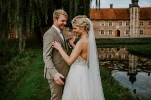 Brautpaar hält Händchen am Teich vor historischer Kulisse – natürliche Hochzeitsreportage NRW.