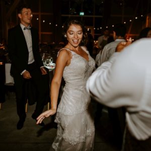 Eine Braut im Spitzenkleid tanzt und lächelt unter Freunden – authentische Hochzeitsreportage NRW.