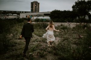 Brautpaar lacht und läuft gemeinsam durch eine wilde Wiese, Hochzeitsfotografin Bonn hält den Moment fest.