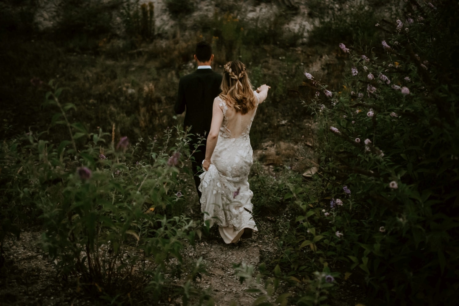 Braut und Bräutigam gehen Hand in Hand durch grüne Natur – echte Hochzeitsreportage NRW.