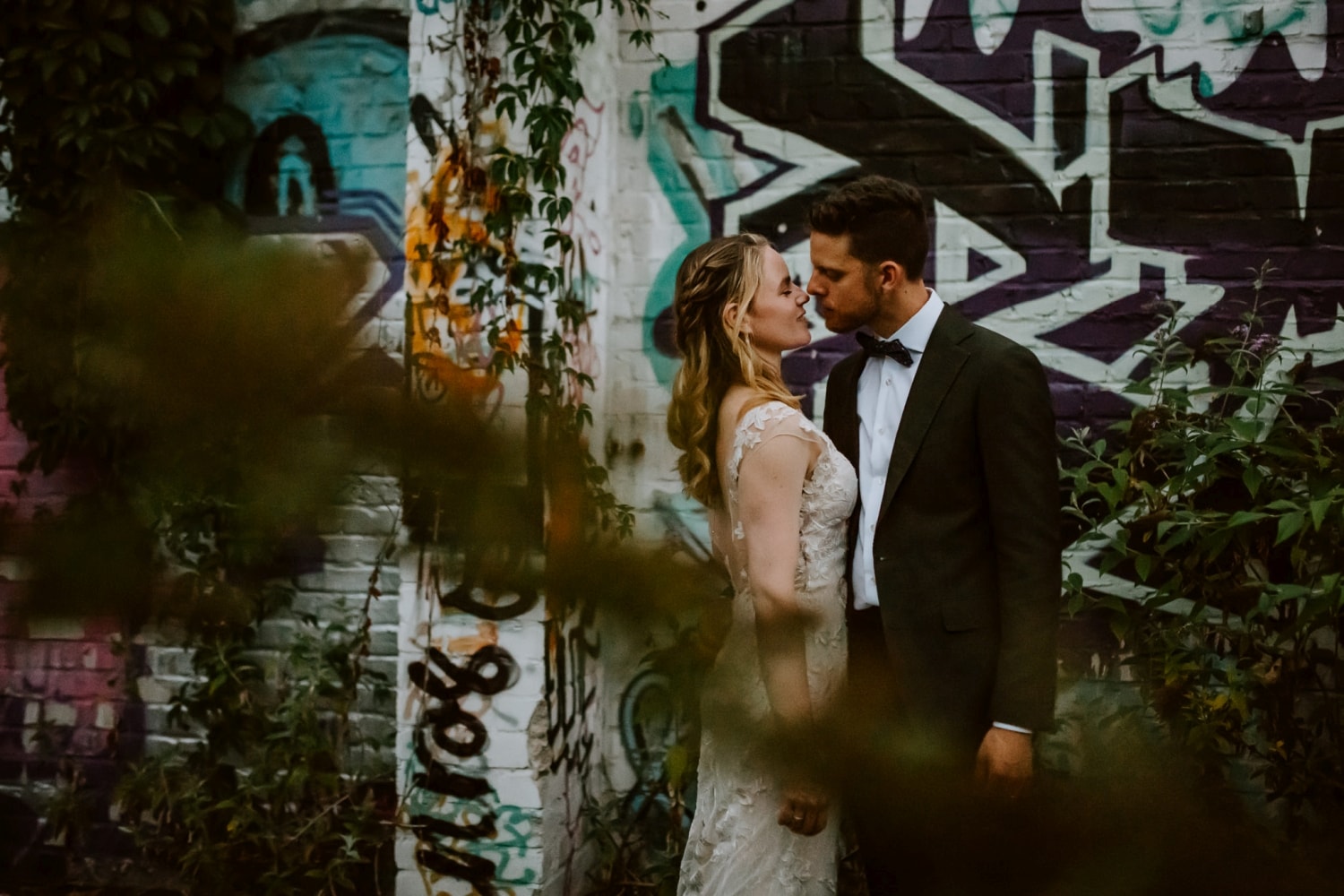 Brautpaar hält sich liebevoll vor einer bunten Wand im Grünen – Hochzeitsfotografin Köln Moment.
