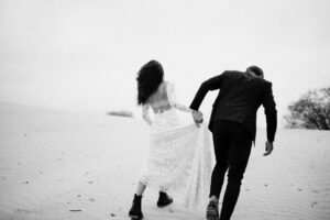 Brautpaar Hand in Hand auf sandigem Weg – festgehalten von Hochzeitsfotografin Köln, schwarz-weiß.