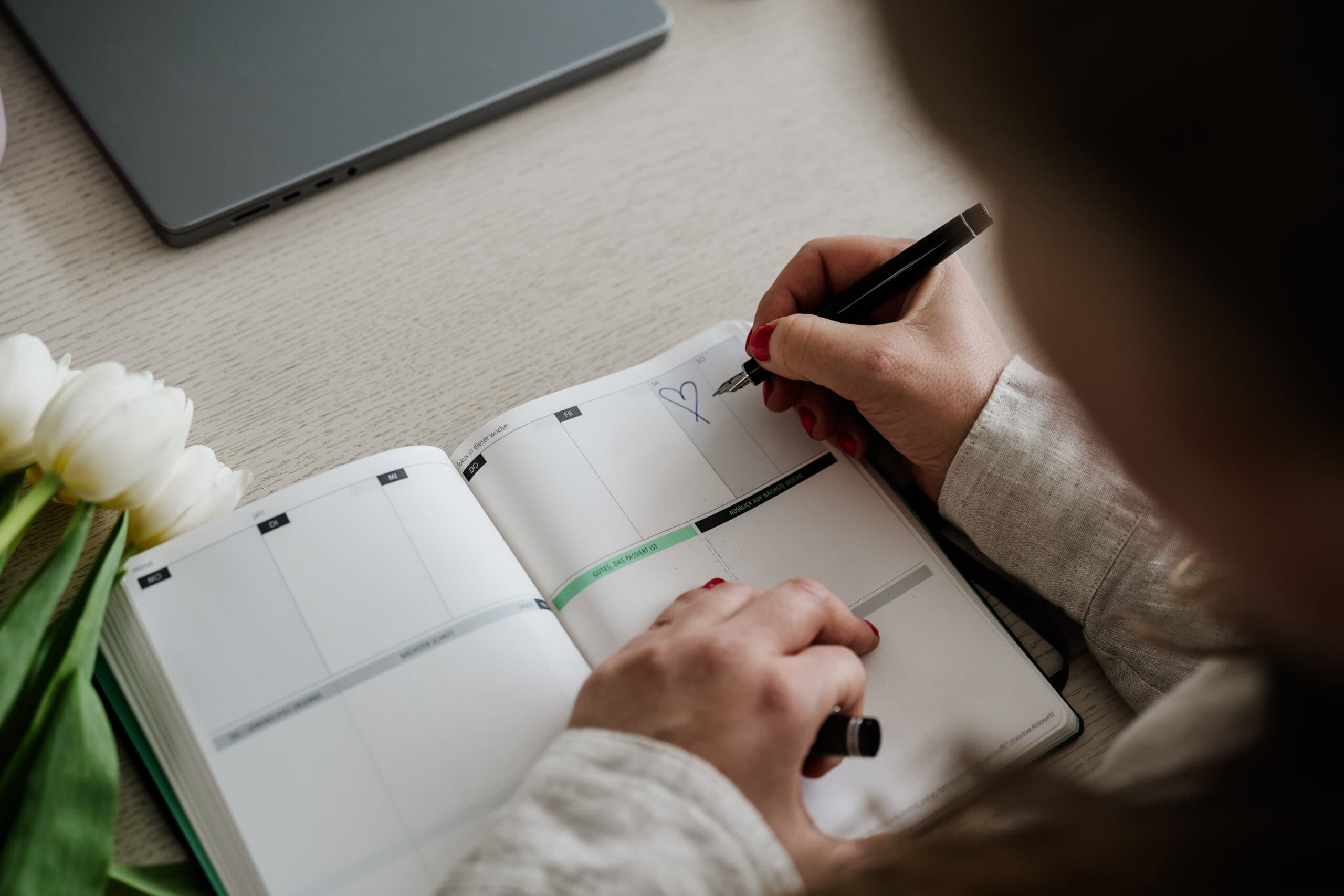 Eine Hand malt ein Herz ins Kalenderblatt; Tulpen und Laptop sorgen für entspannte Hochzeitsvorfreude.